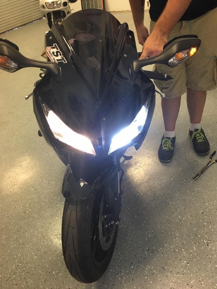 Black sport motorcycle with bright headlights parked indoors, with two people standing beside it.