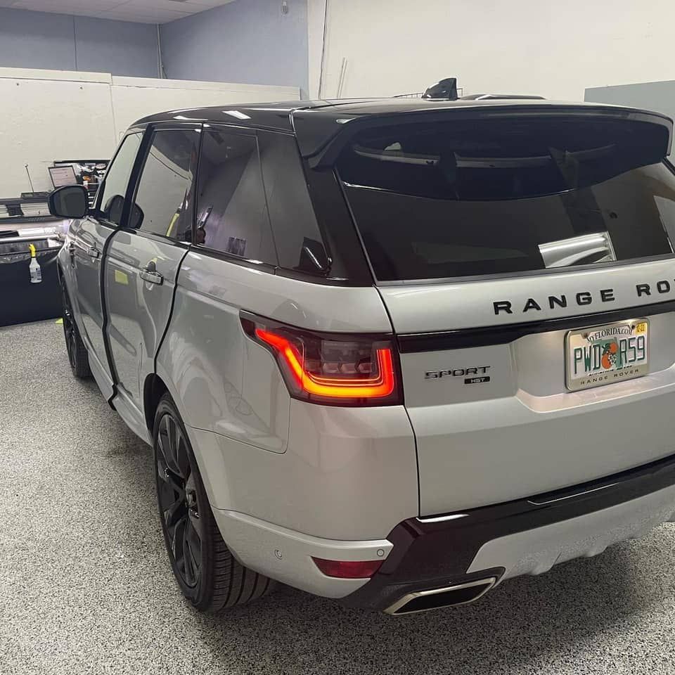 Silver Range Rover SUV parked indoors in a garage, rear view with taillights on.