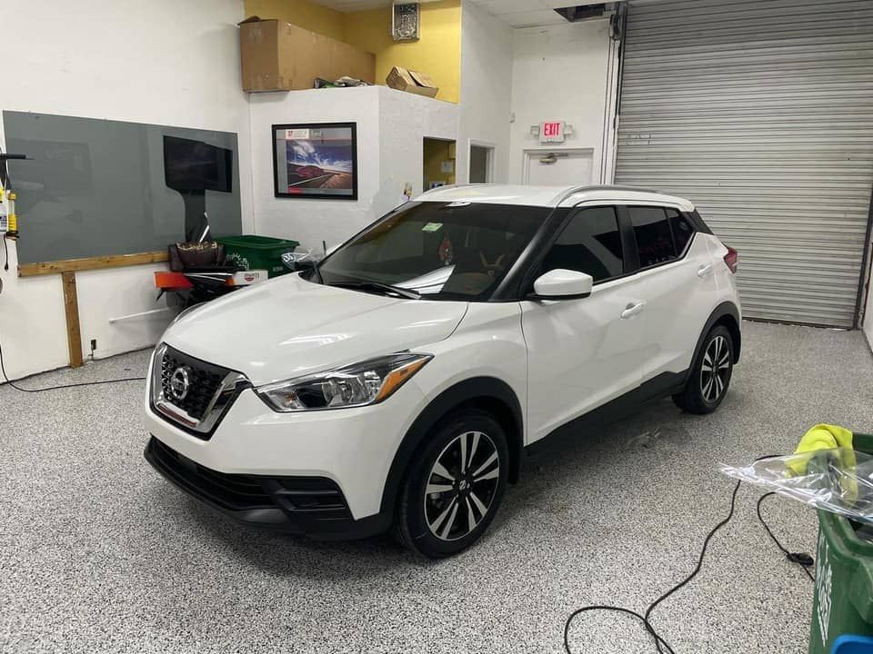 White Nissan SUV in a garage, angled front view with tools and a roll-up door in the background