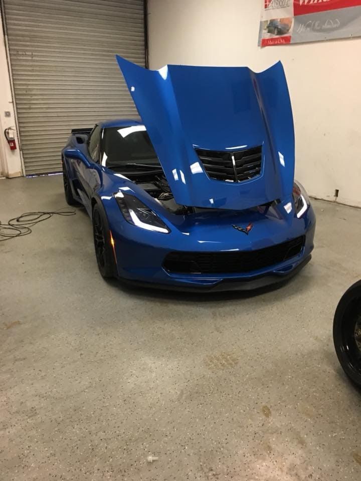 Blue sports car in a garage with hood open, showing the engine area.