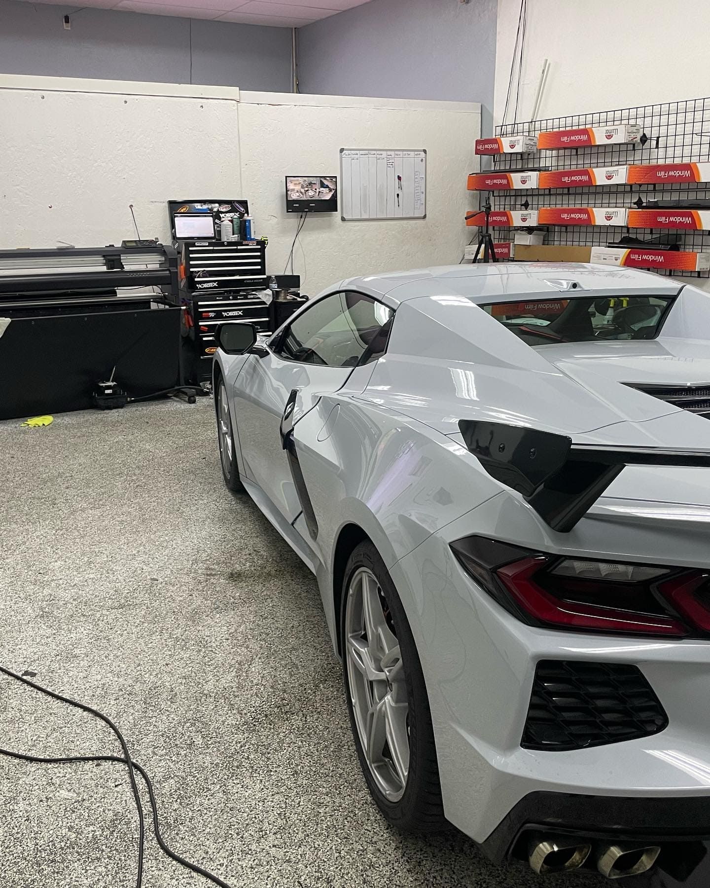 Silver sports car in a garage workshop with shelves, tools, and equipment in the background