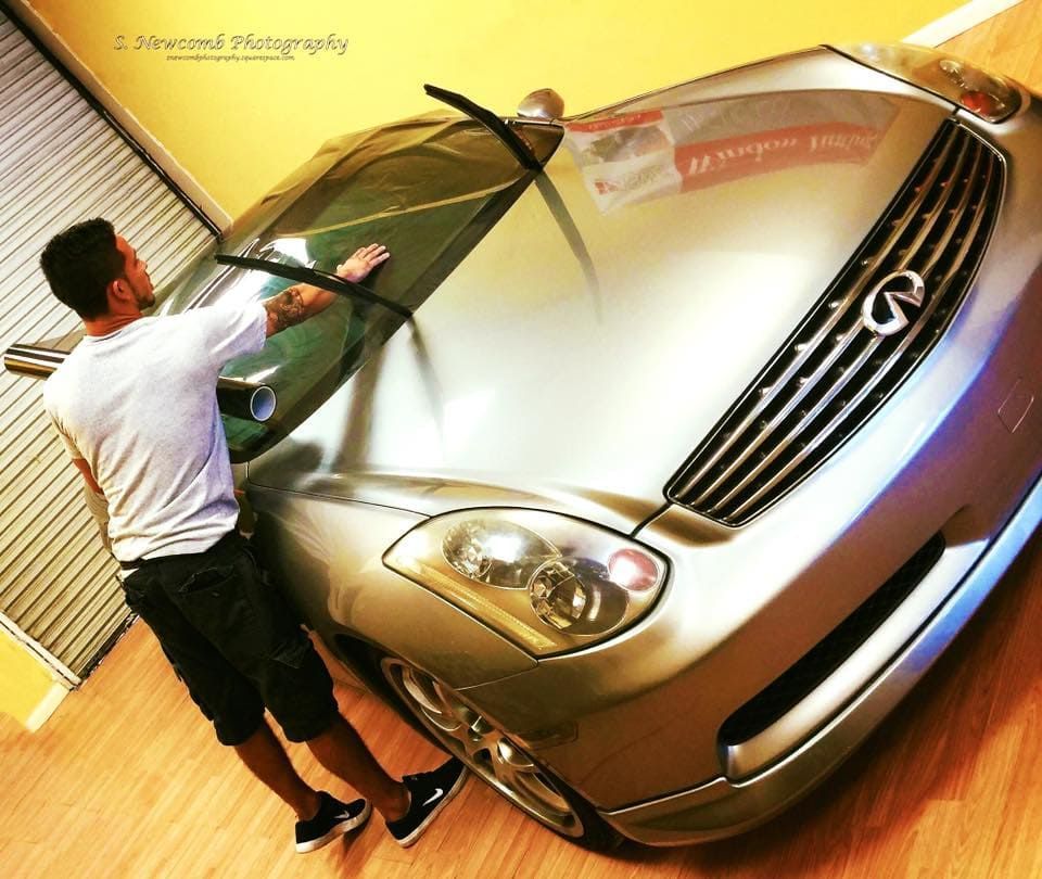 Man washing a silver car with a hose in a garage-like setting