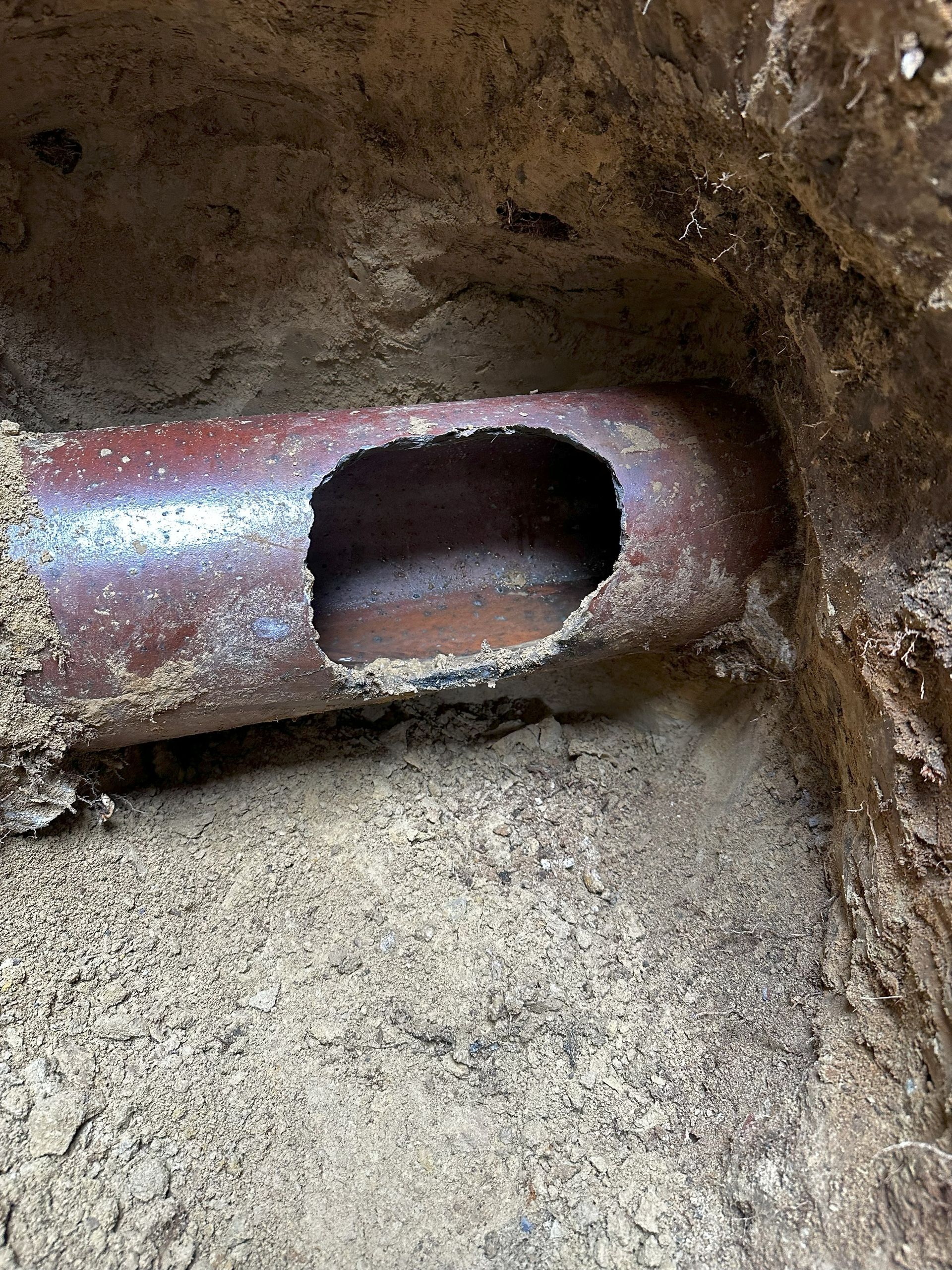 PVC pipe repair in a sandy trench. Tools, including a hammer and pliers, are nearby.