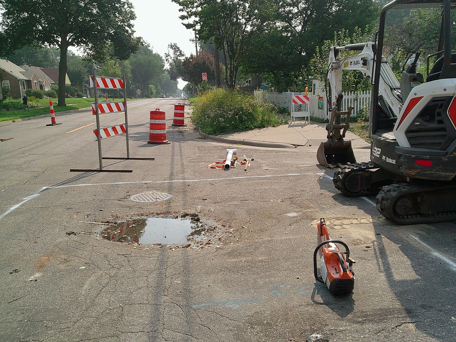 Road construction site: excavator, barriers, and orange cones on a street with a pothole.