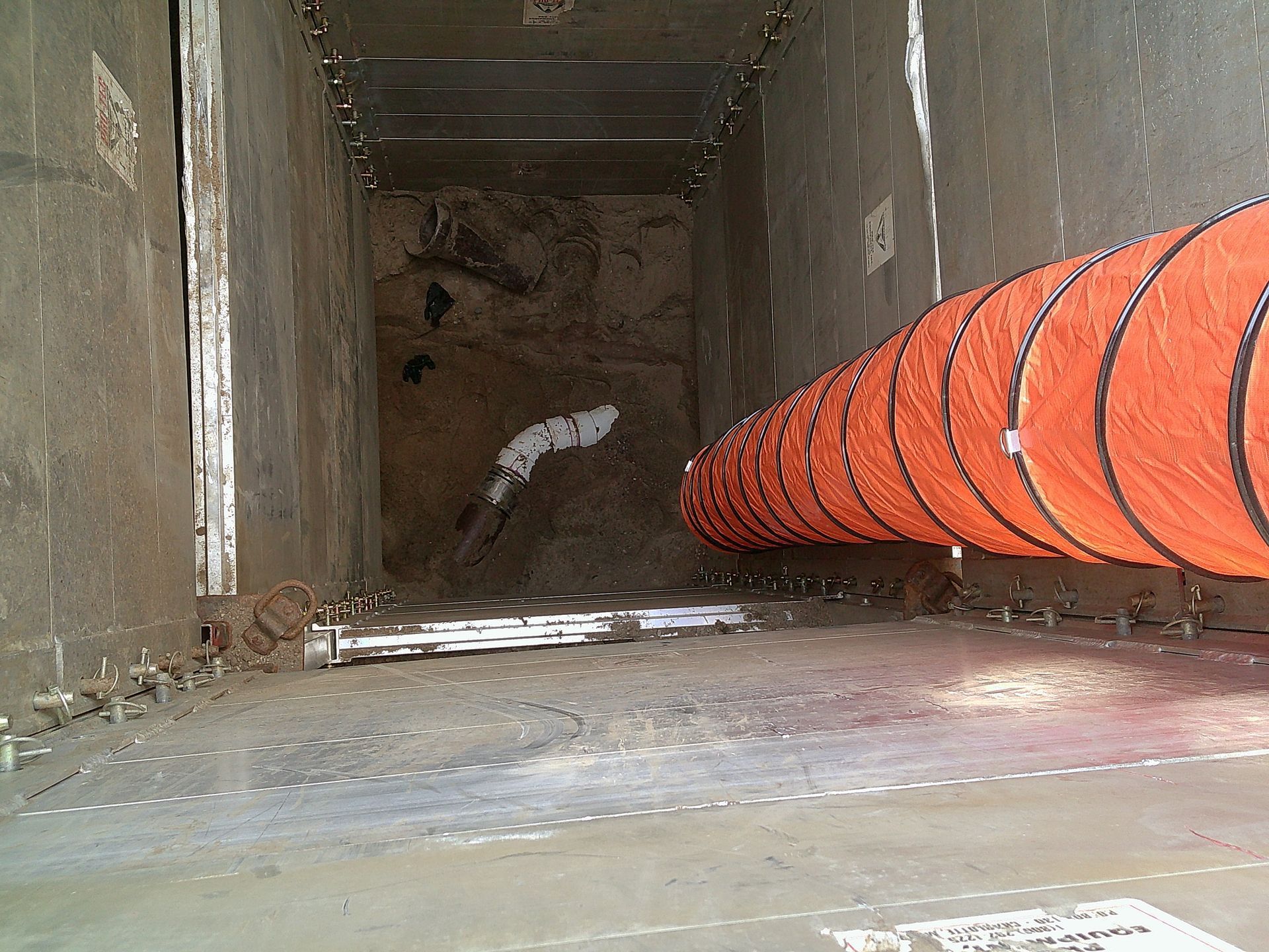Inside a confined space, orange ventilation tube extends toward a dirt pile. Concrete walls.