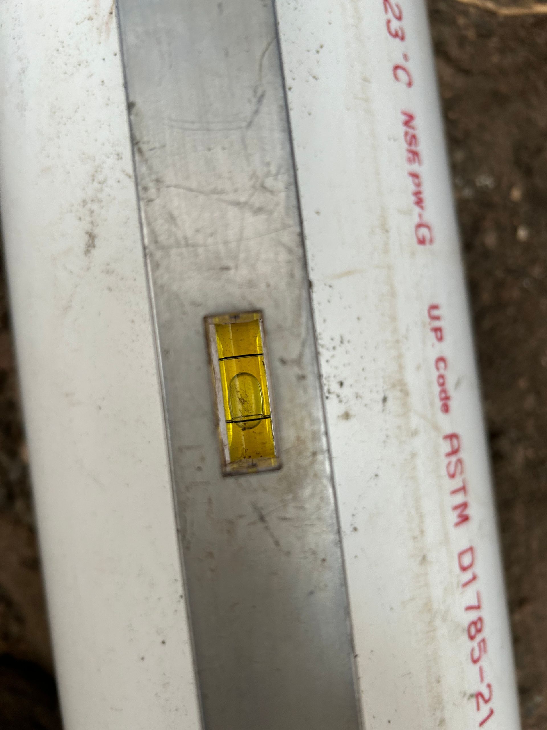 A level mounted on a white PVC pipe; the bubble is centered, indicating level.