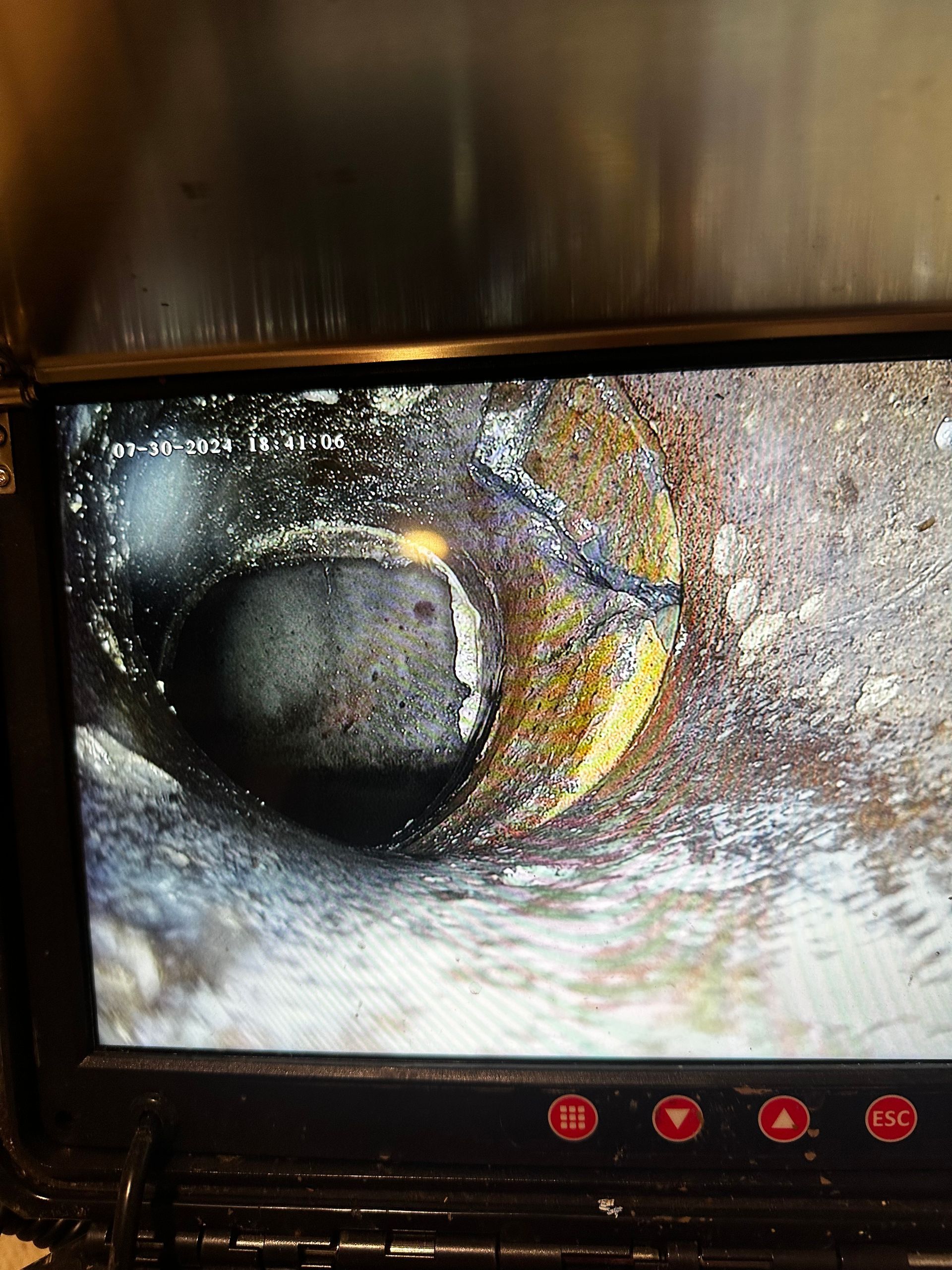 Camera view inside a corroded pipe, showing a dark, circular opening surrounded by rust and debris.