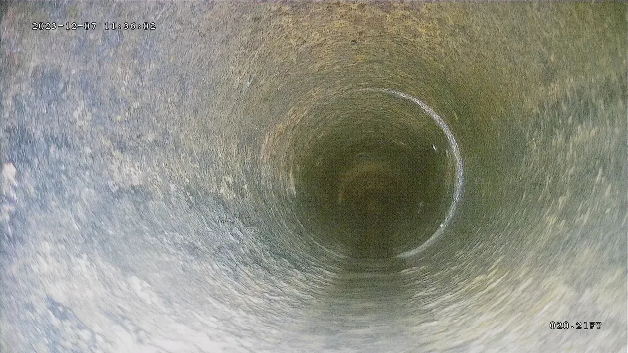 Inside view of a pipe, showing its circular interior. Gray and white hues are visible, with some debris.