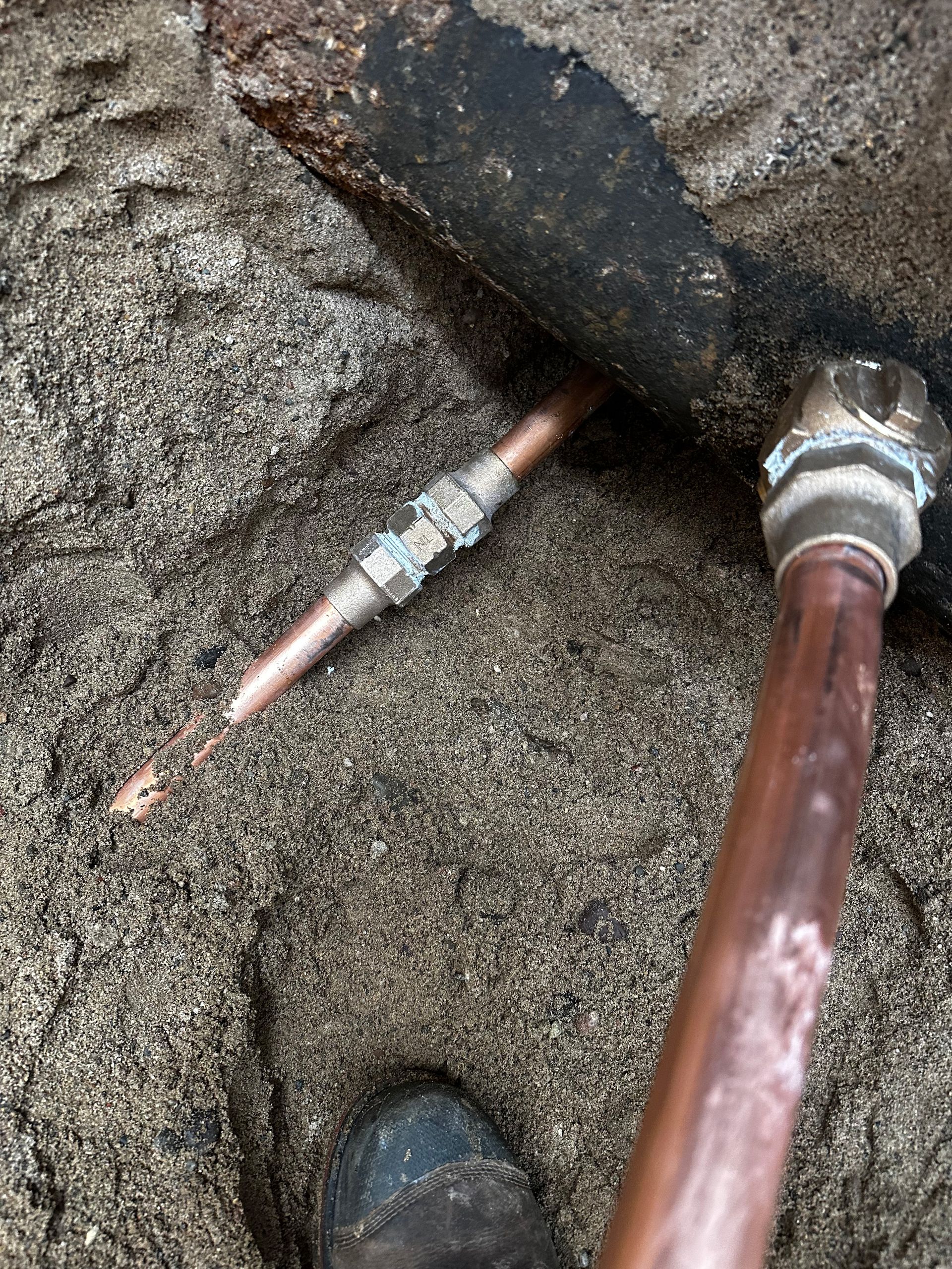 Copper pipes and fittings partially buried in sand, with a boot visible.