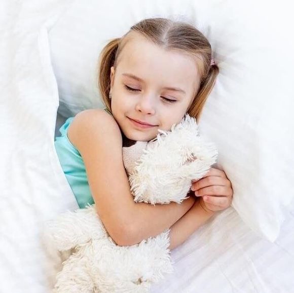 Sleeping child hugging a white teddy bear on a bed with white pillows