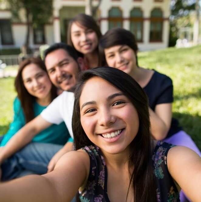 Group of five smiling friends taking a selfie outdoors in front of a building