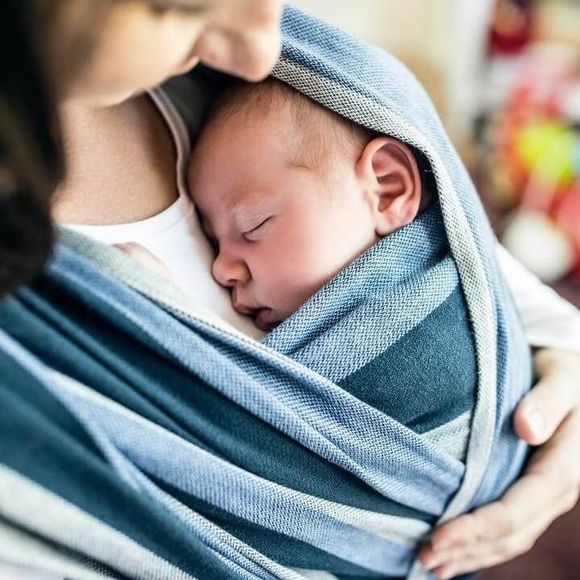 Sleeping baby wrapped in blue fabric, cradled in an adult’s arms