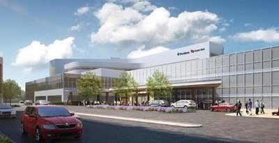 Modern hospital exterior with glass facade, parked cars, and people entering under a cloudy sky