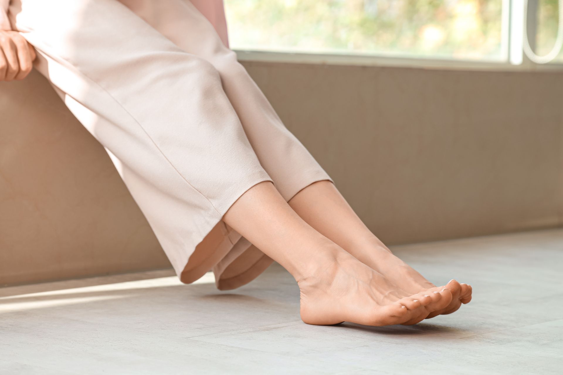 A woman is sitting on a window sill with her legs crossed.