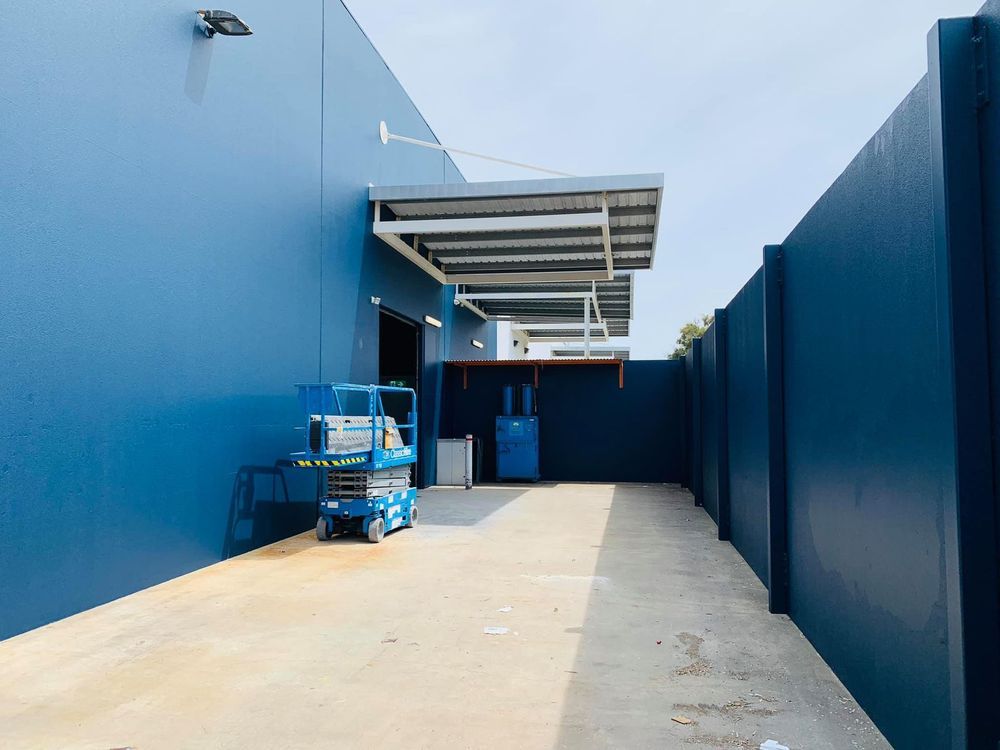 Blue industrial corridor with a covered loading area and a cart near the entrance