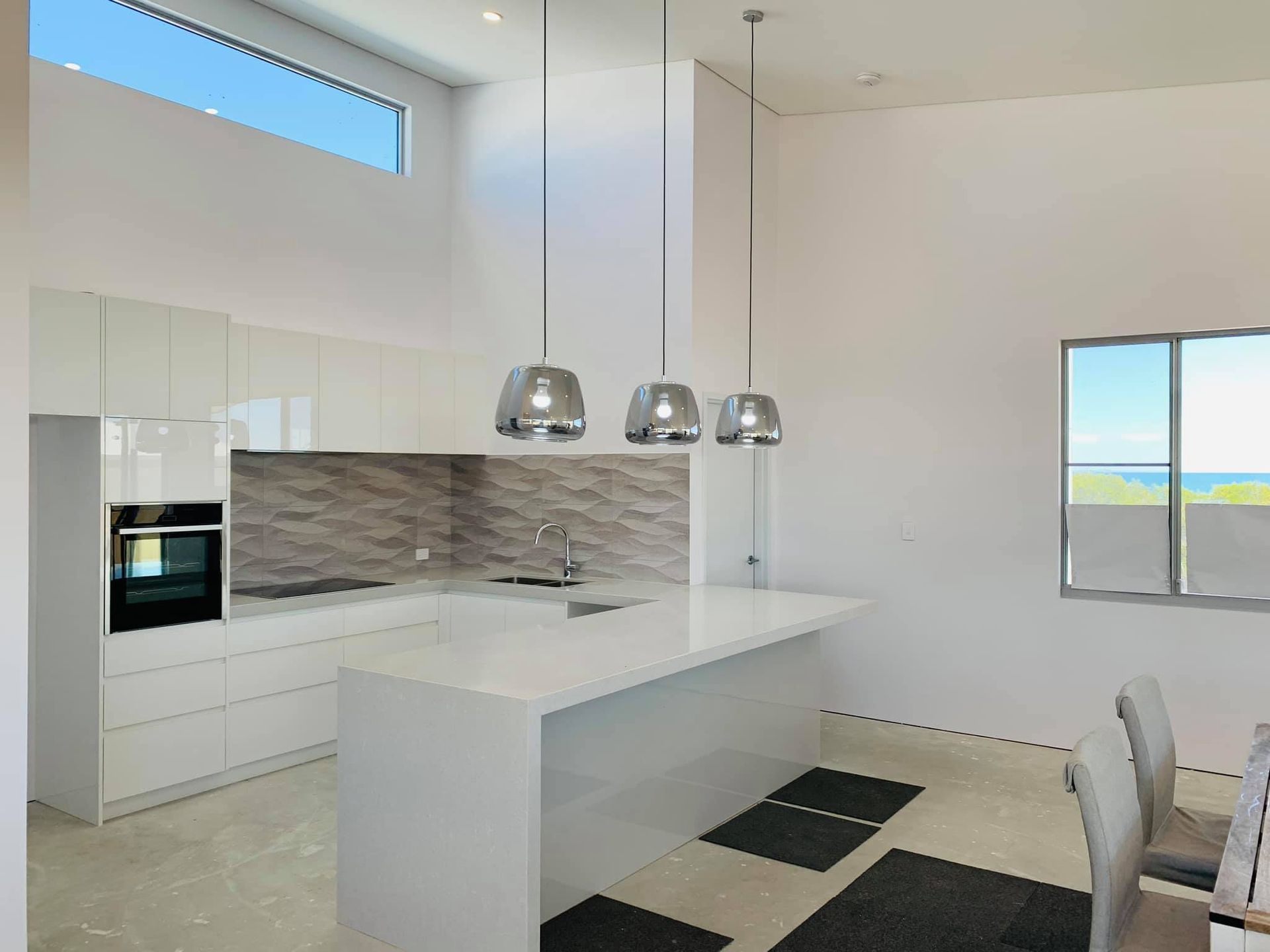Modern white kitchen with island, pendant lights, glossy cabinets, and gray backsplash
