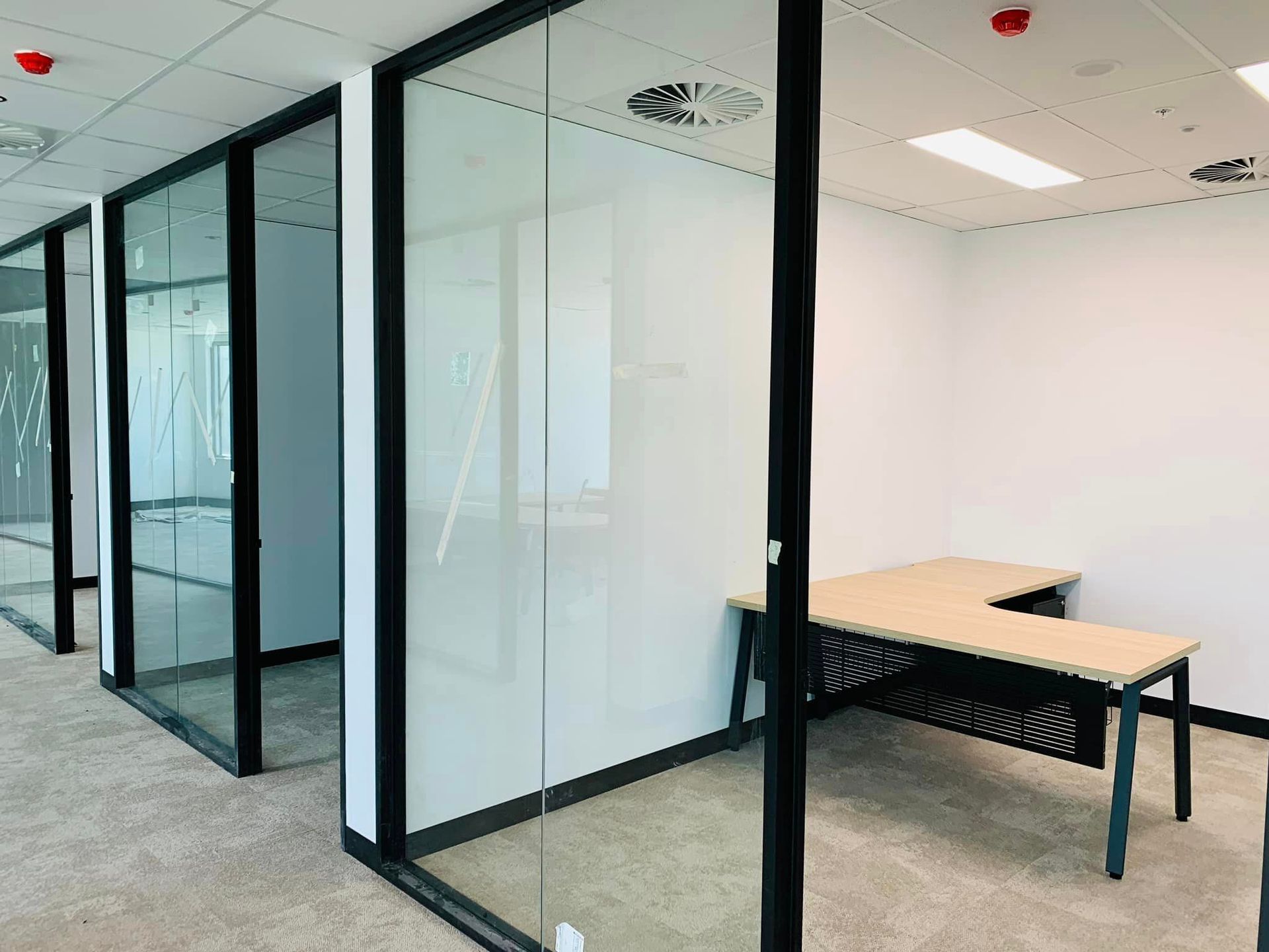 Modern office interior with glass meeting rooms, black frames, and desks on a gray carpet