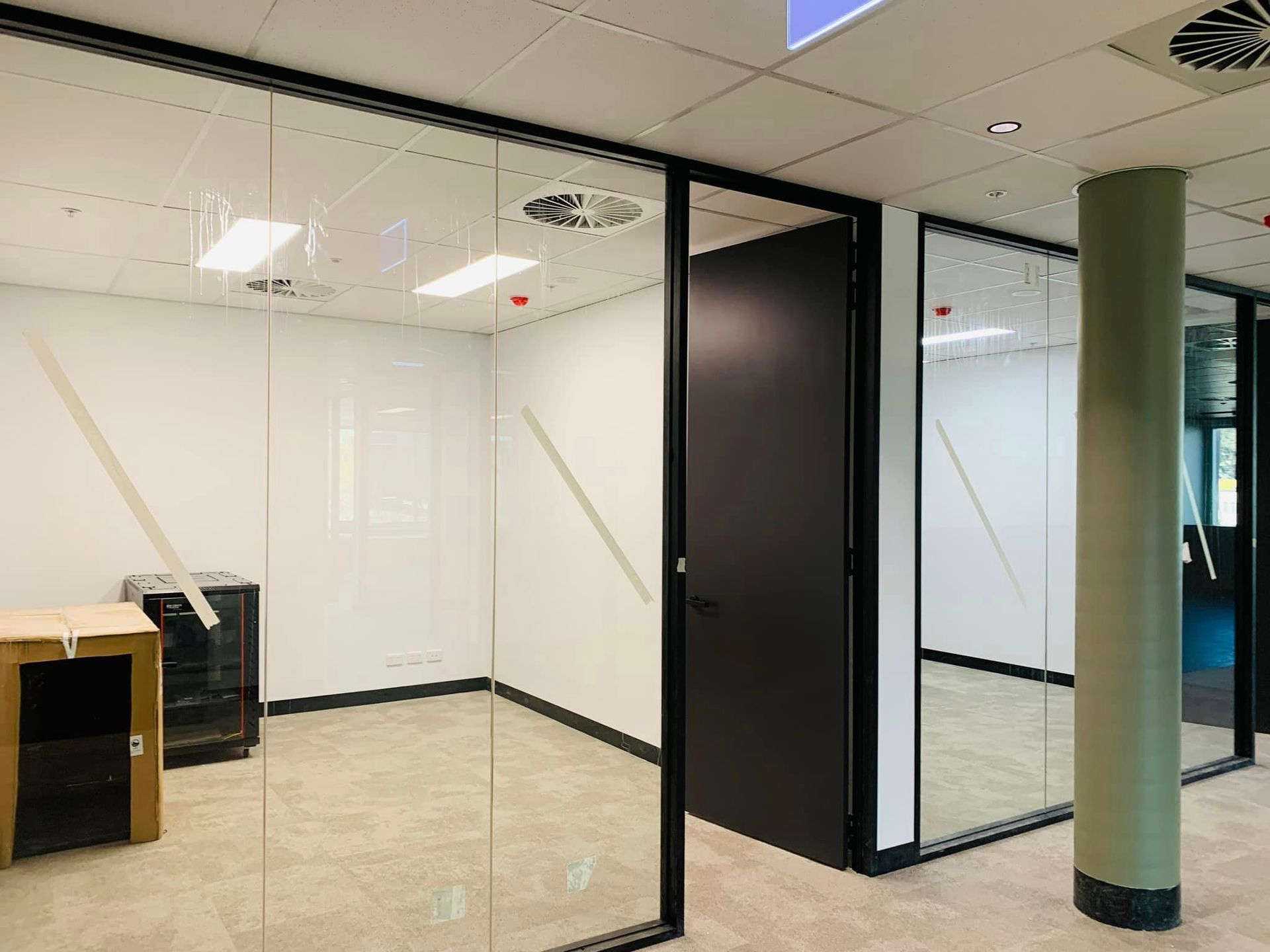 Empty modern office with glass partitions, white walls, tiled floor, and a green support column
