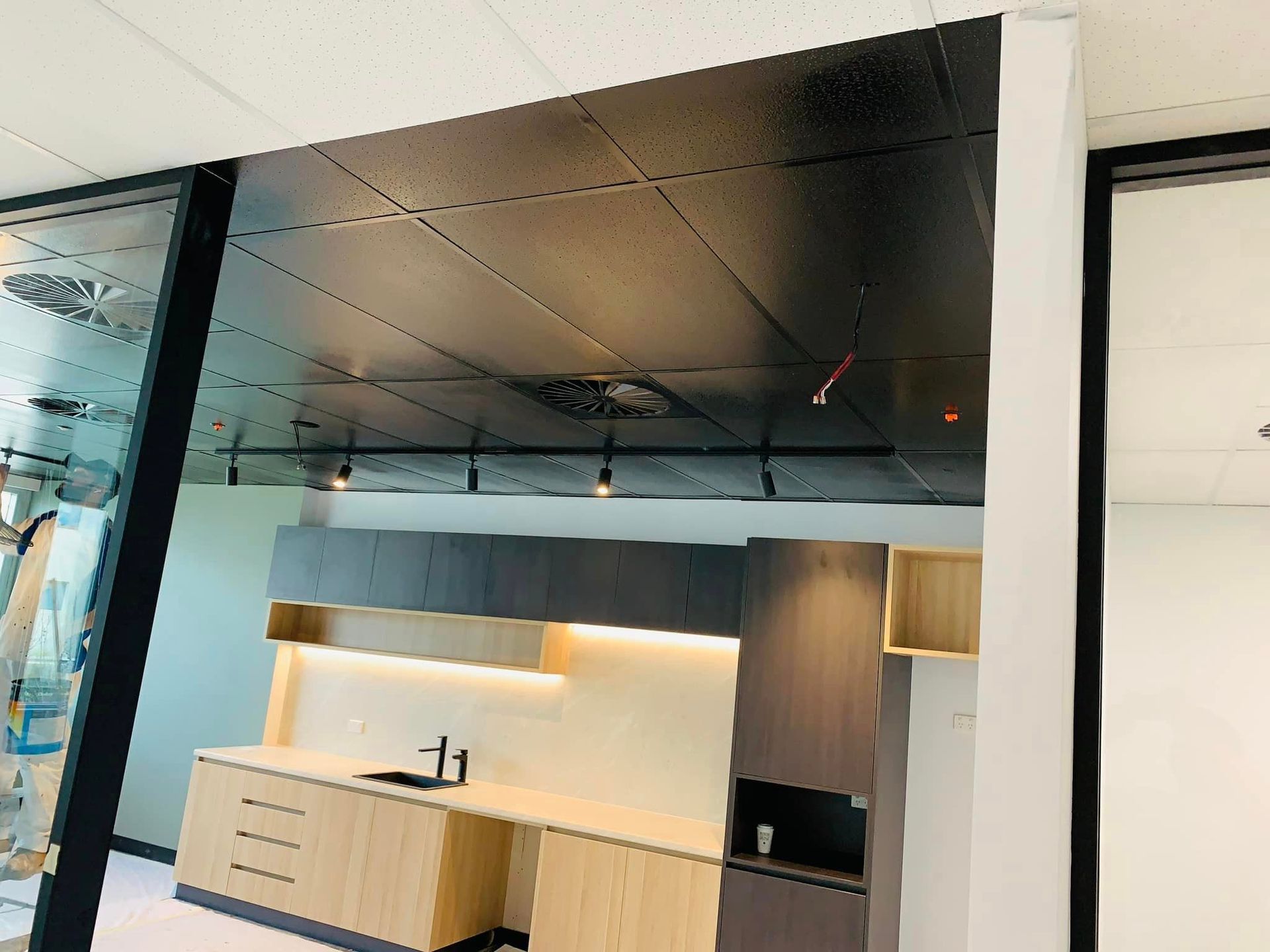 Modern kitchenette with black ceiling, wood cabinets, white countertop, and built-in sink under warm lighting