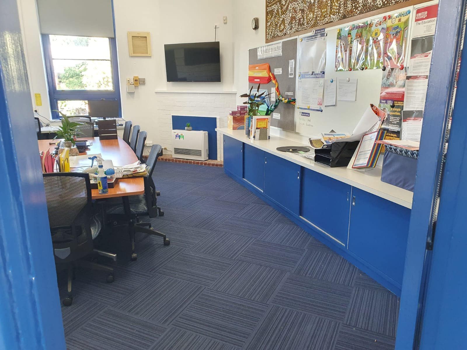 Classroom with blue cabinets, desks, wall-mounted TV, and children’s artwork display