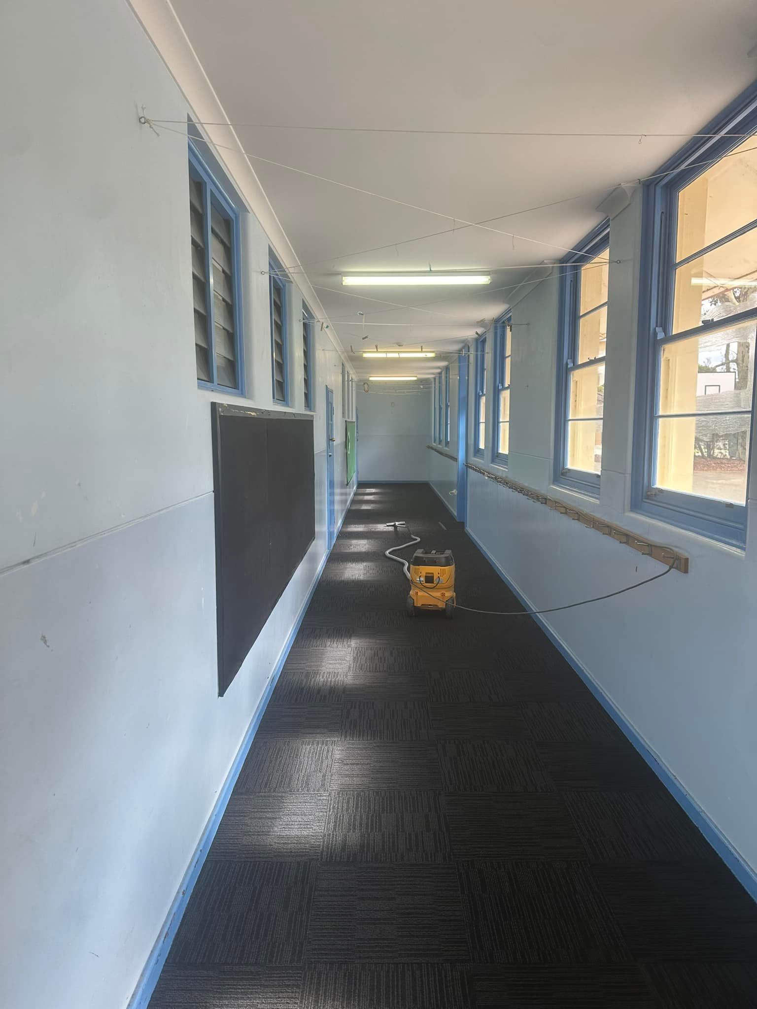 Empty school hallway with blue windows and a wet black floor, a small yellow cart in the center.