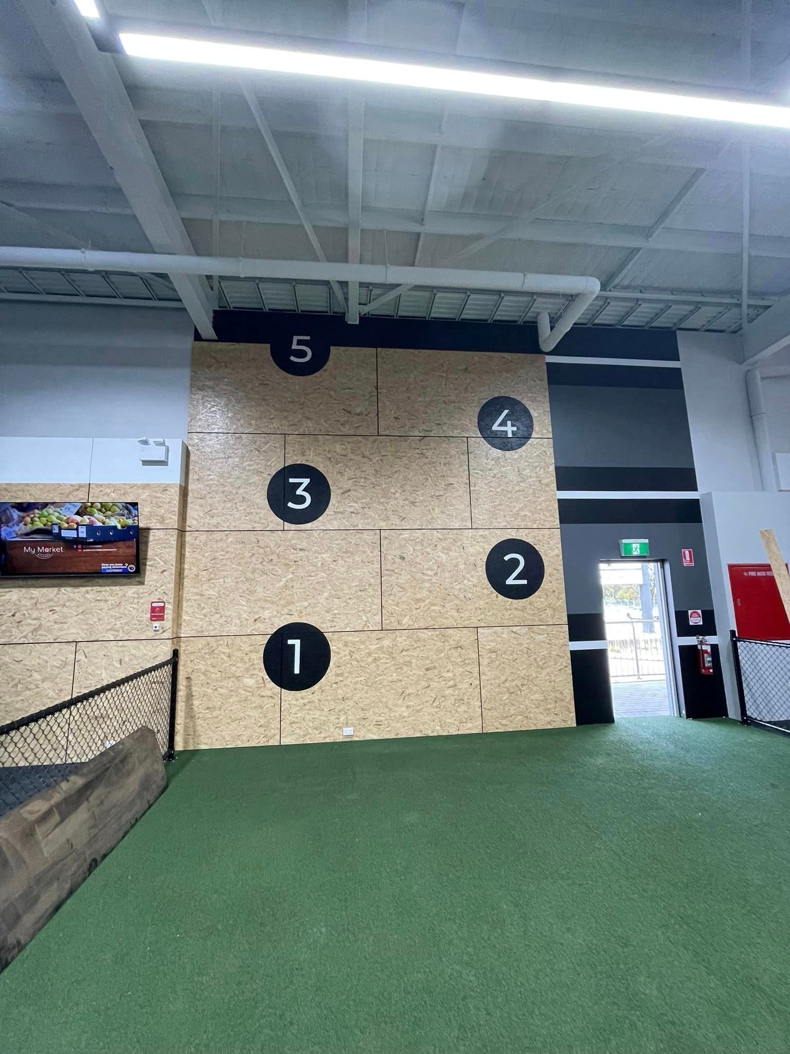 Indoor gym wall with numbered black targets and green turf floor