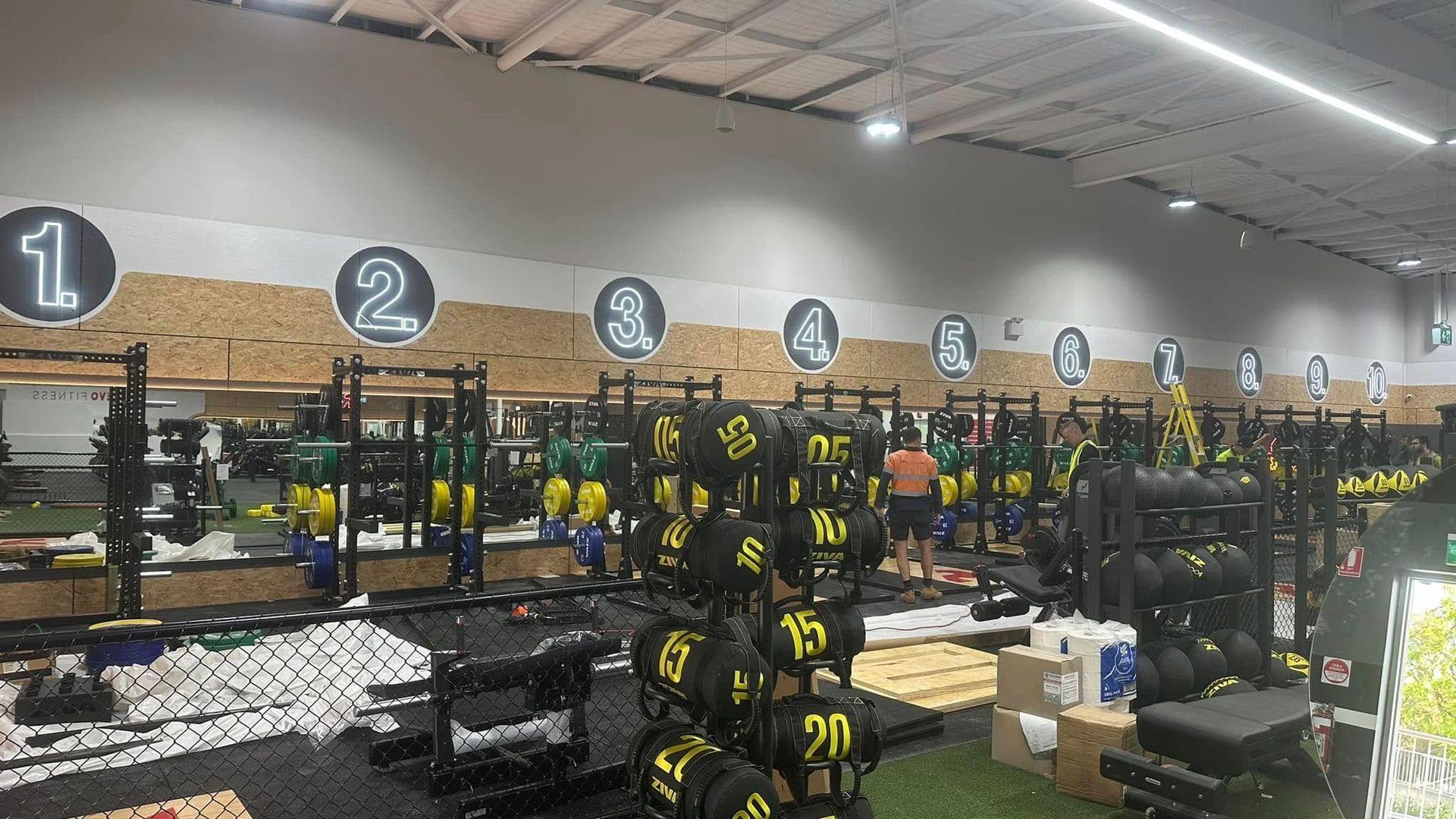 Indoor retail store with numbered sections, shelves of yellow-and-black gear, and boxes on tables under bright lights