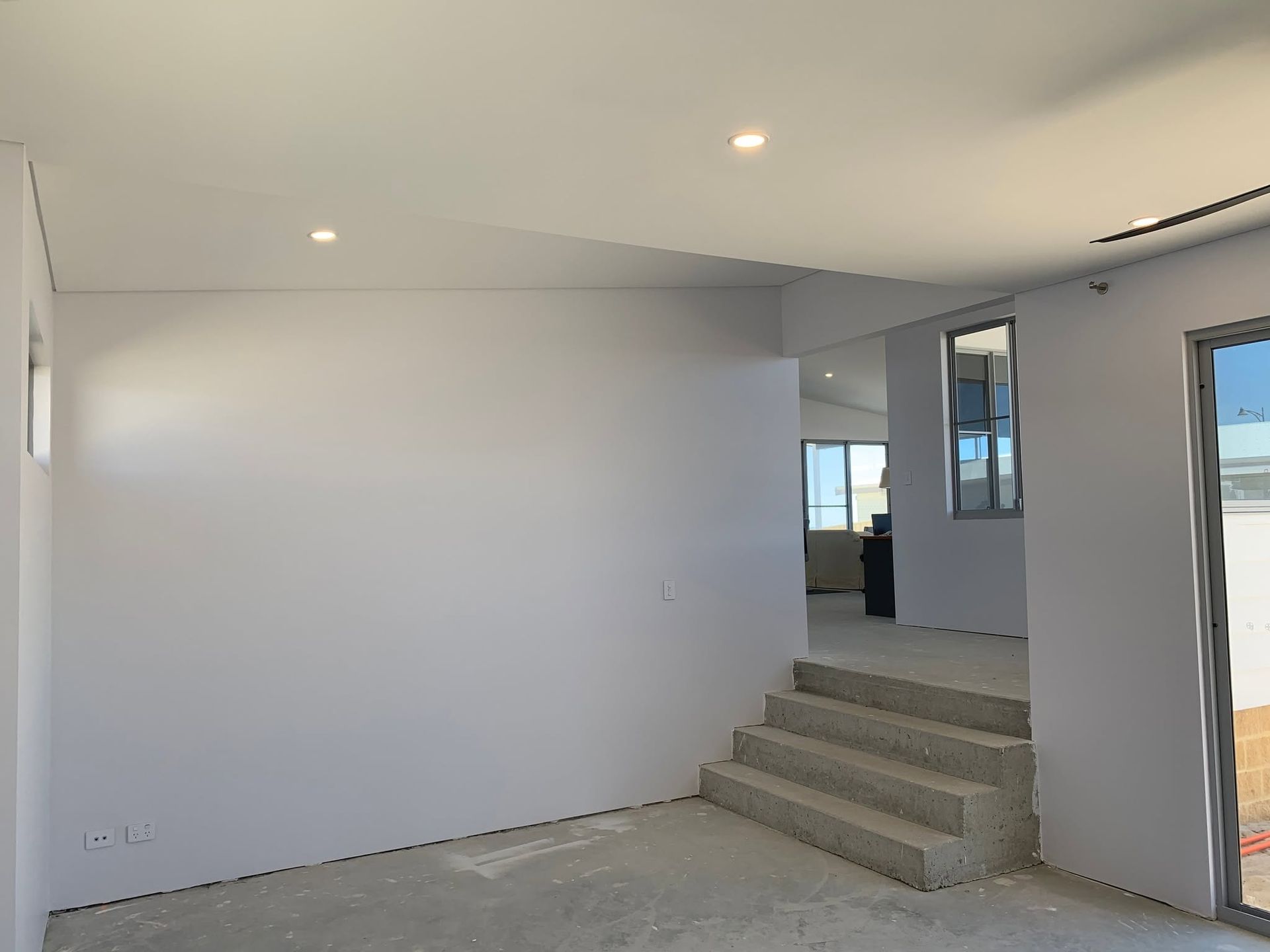 Empty modern room with white walls, recessed lights, and steps leading to an open doorway.