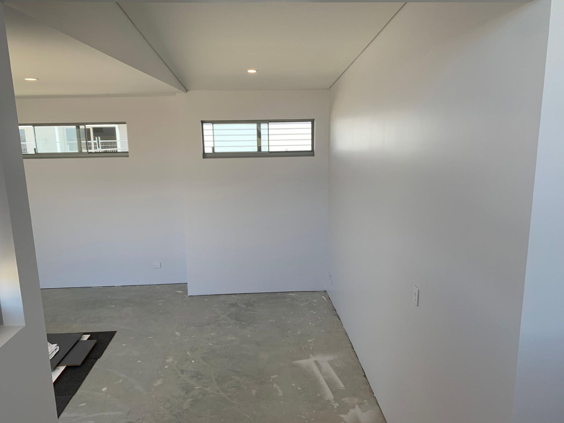 Empty unfinished room with white walls, gray floor, and two small horizontal windows.