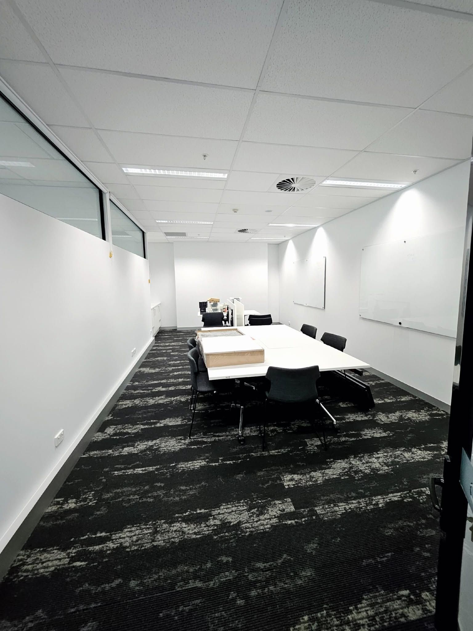 Empty modern office meeting room with white walls, black carpet, and tables with chairs
