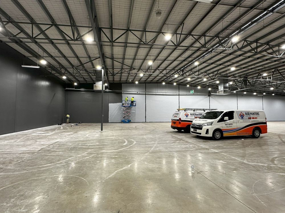 Large empty warehouse with high lights, two vans parked on the right, and a reflective concrete floor.