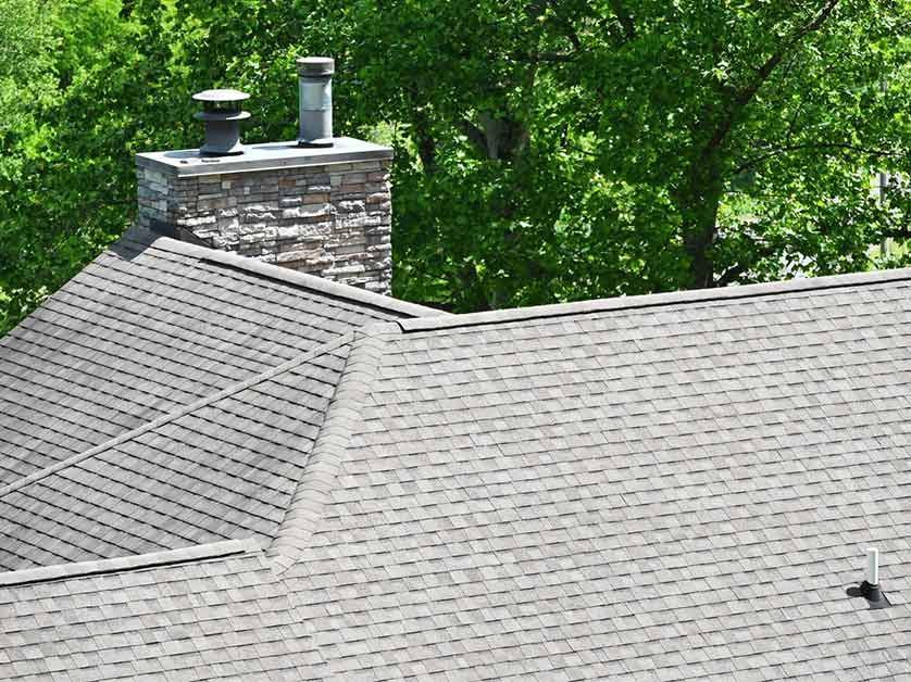 A roof with a chimney on top of it and trees in the background.