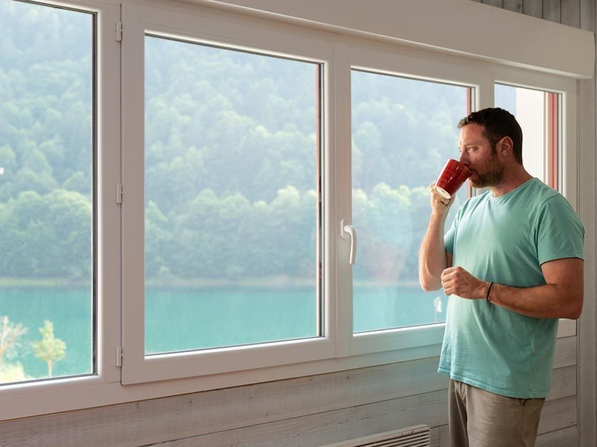 A man is drinking a cup of coffee while looking out a window.