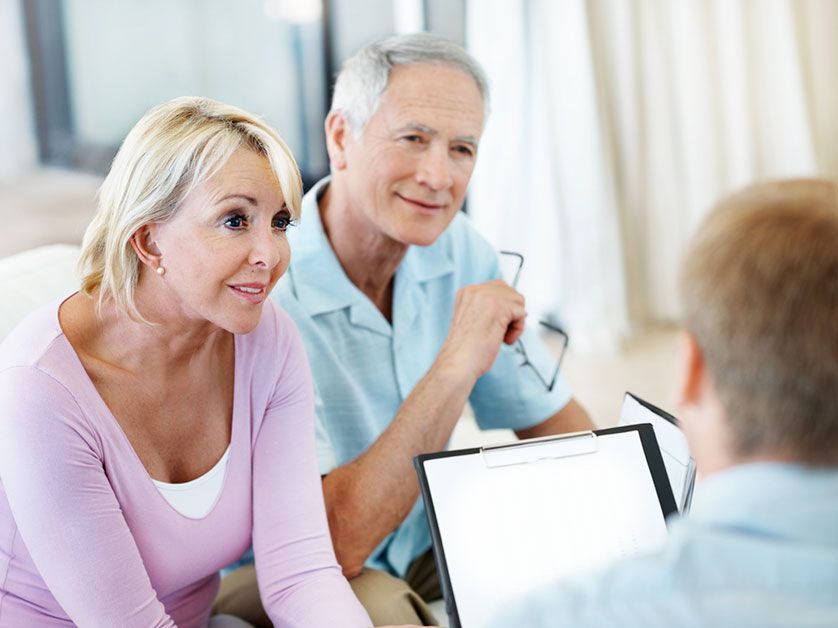 An elderly couple is sitting on a couch talking to a man.