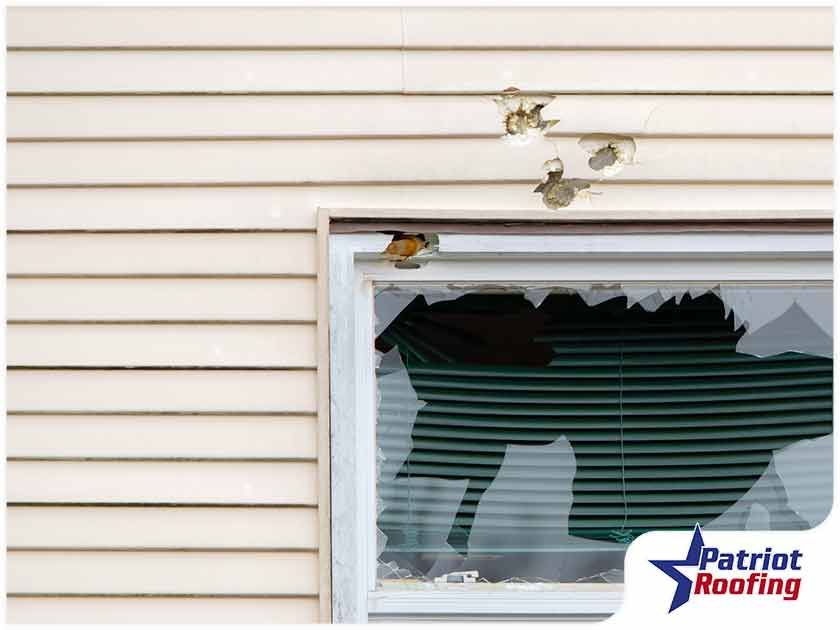 A house with a broken window and a patriot roofing logo
