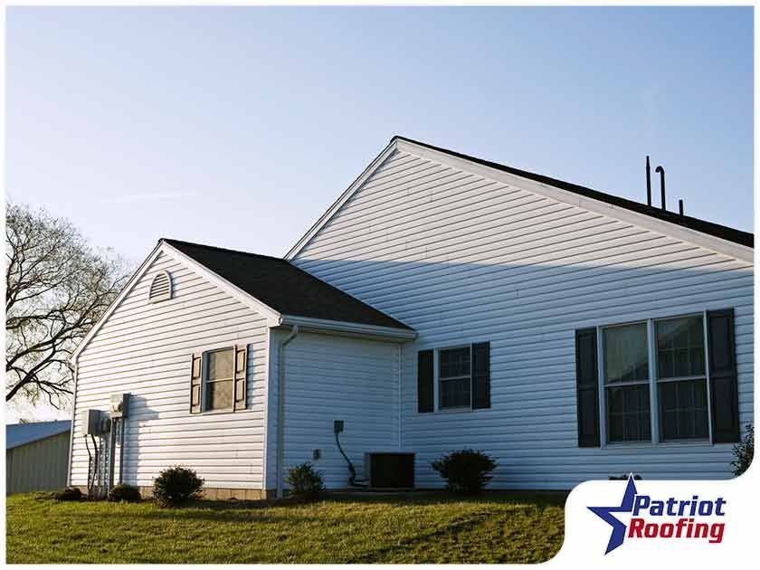 A white house with a black roof and a patriot roofing logo