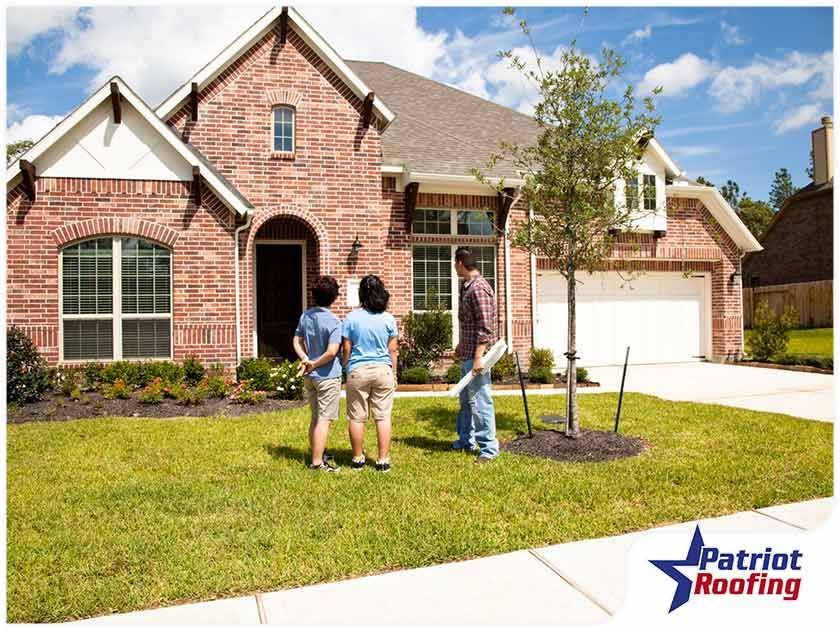 A group of people standing in front of a brick house with patriot roofing in the corner