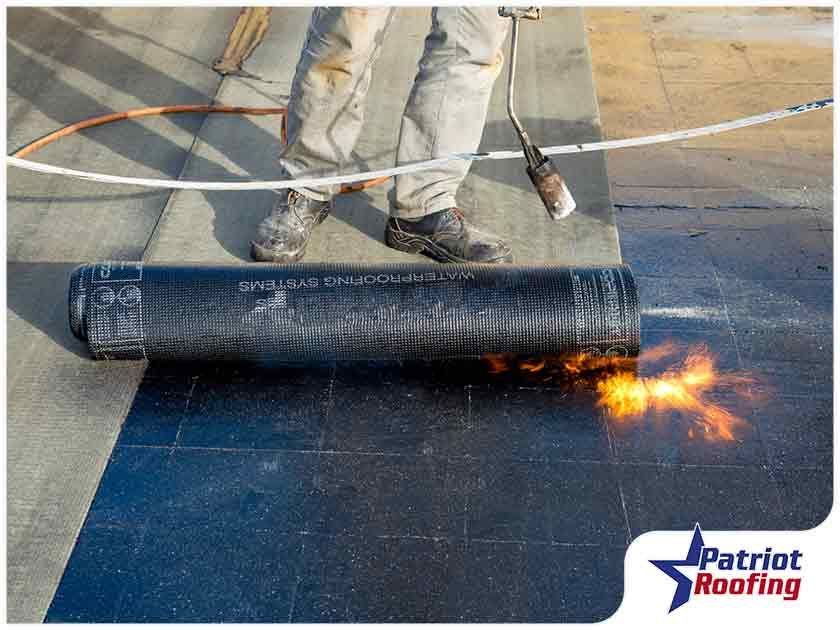 A person is rolling a roll of roofing material on a roof.