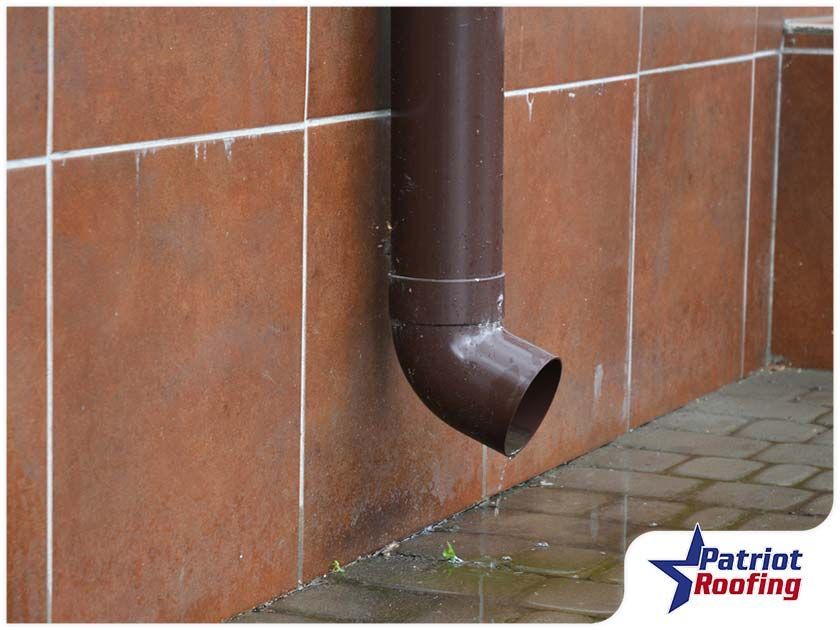 A brown drainpipe is hanging from a tiled wall.