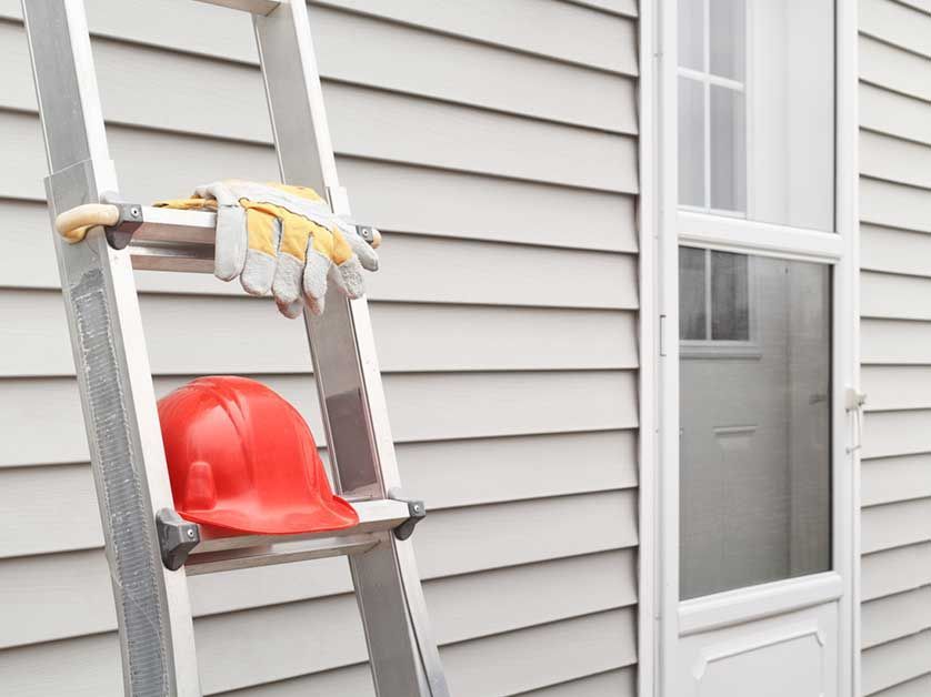 A red hard hat and gloves are hanging on a ladder.