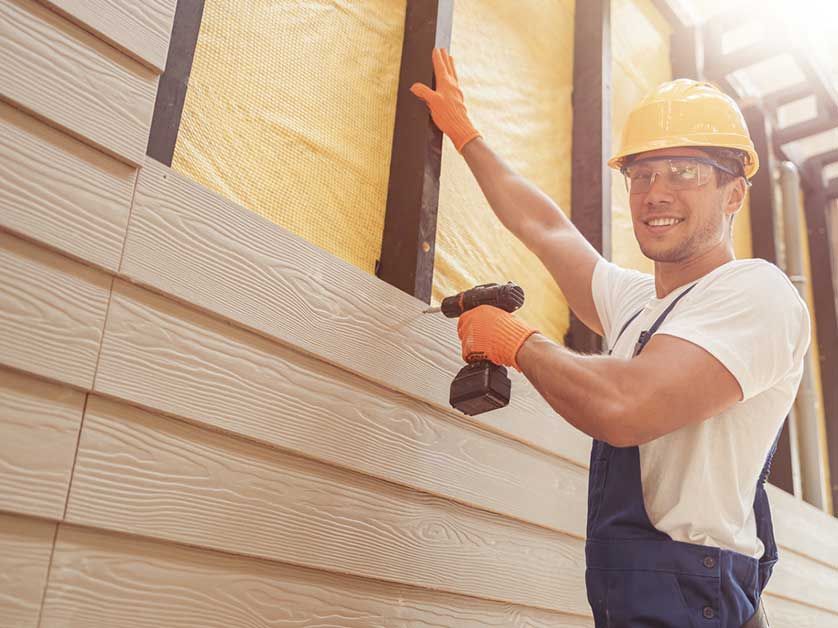 A man is installing siding on a house with a drill.