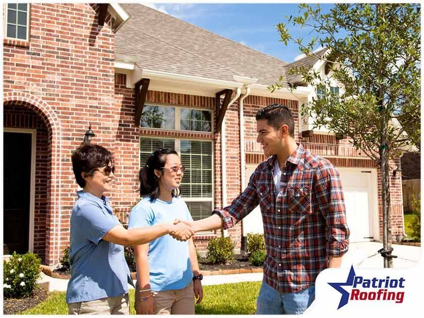 A man and two women are shaking hands in front of a brick house.