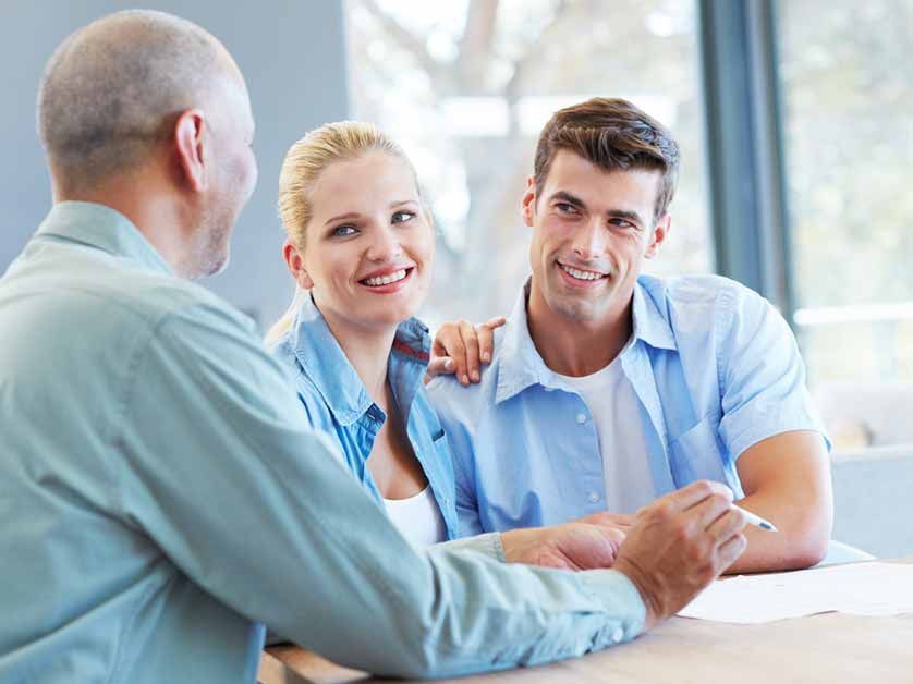A man and a woman are sitting at a table talking to a man.