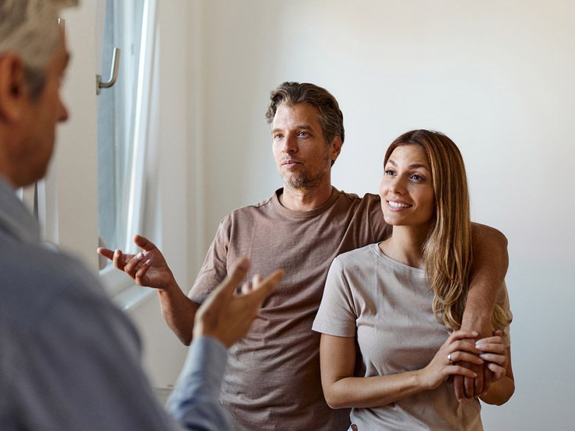 A man and a woman are standing next to each other in a room talking to a real estate agent.