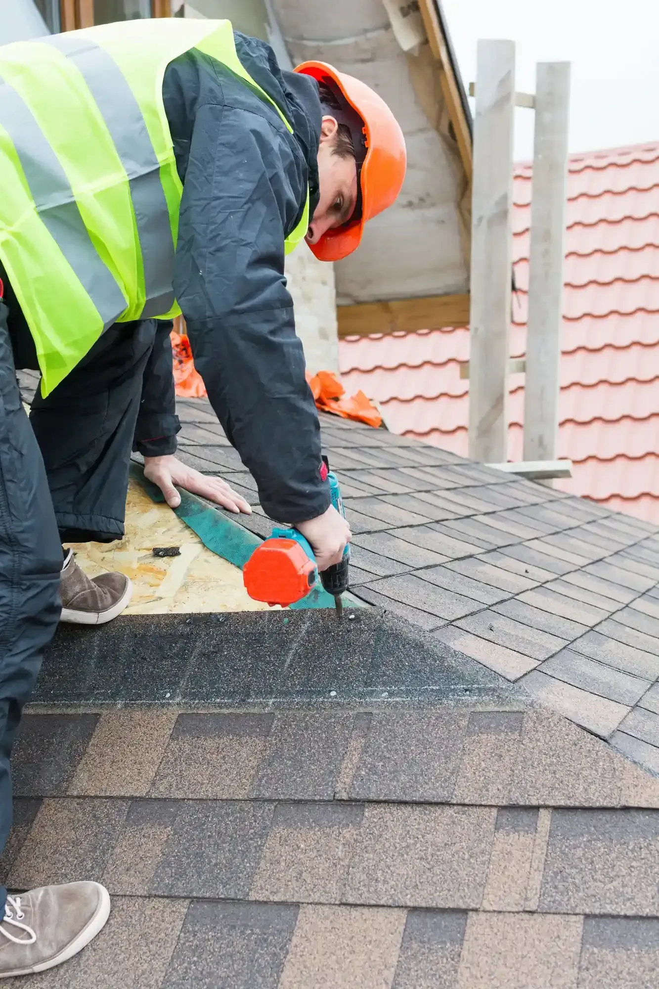 A man wearing a hard hat and safety vest is working on a roof.