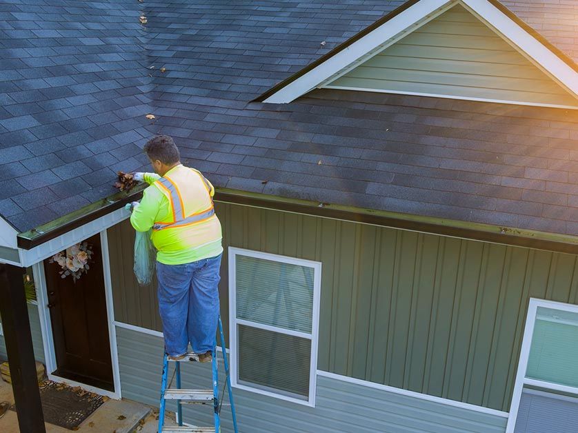A man is standing on a ladder working on the roof of a house.