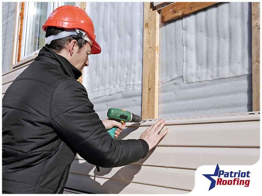 A man is installing siding on a house with a drill.