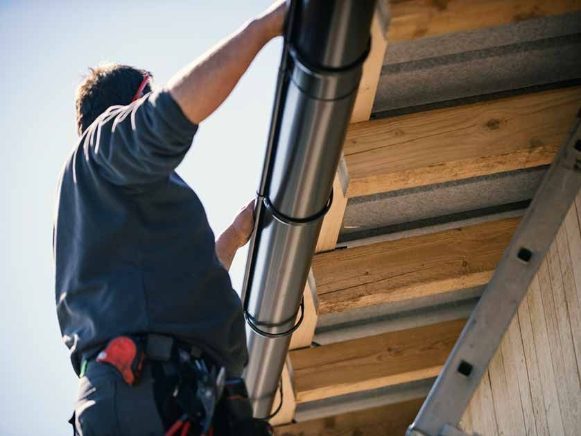 A man is installing a gutter on the side of a building.