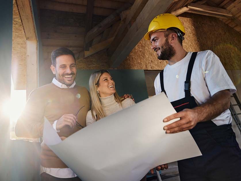 A man and a woman are looking at a blueprint with a construction worker.