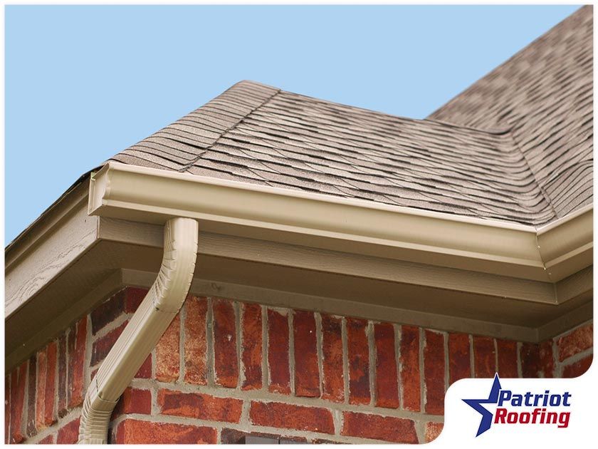 A gutter on the side of a brick building with patriot roofing written on the bottom
